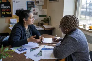 Two women in discussion at a table in a community room, working together in a warm, softly lit setting with a natural, candid atmosphere.